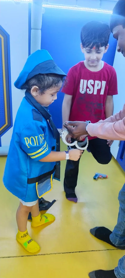 A child in a police costume is being handcuffed by an adult, while another child watches.