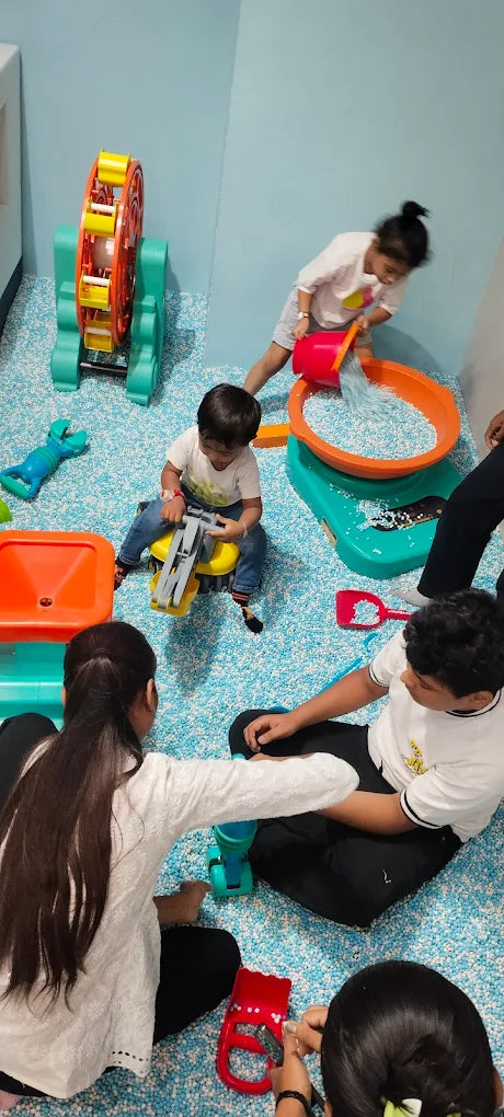 Children play in a ball pit with toys, including a Ferris wheel and a toy truck.