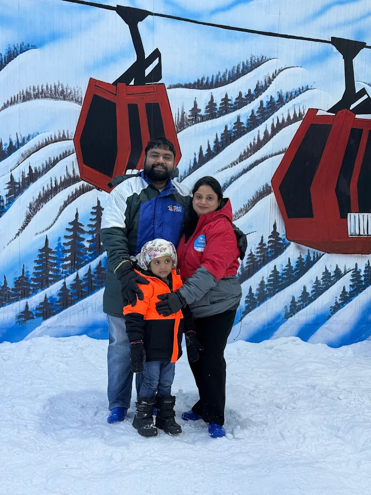 A family poses in the snow in front of a painted ski resort backdrop.