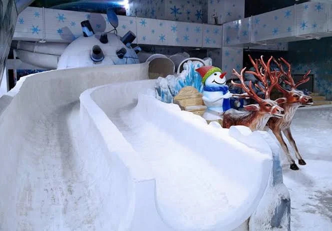 A snowy amusement park slide with a snowman and reindeer decorations.