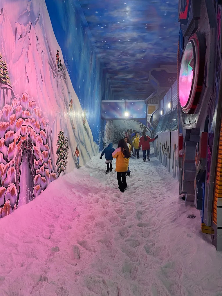 Children walk through a snowy indoor attraction with painted mountain and starry sky walls.