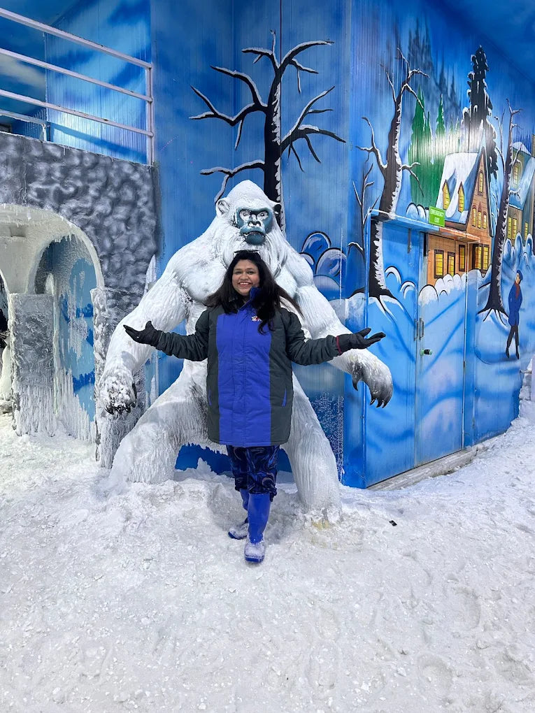A woman poses in front of a yeti statue in a snowy, winter-themed attraction.