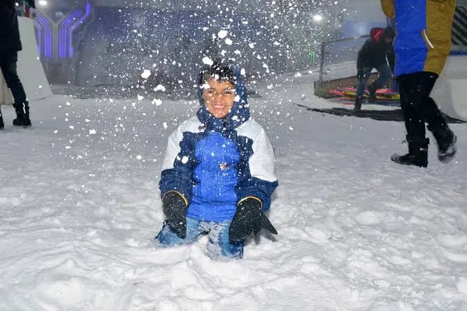 A young child smiles while playing in the snow, surrounded by falling snowflakes.