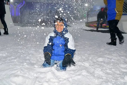 A young child smiles while playing in the snow, surrounded by falling snowflakes.