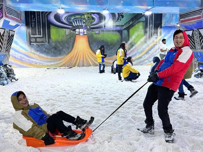 Young adults enjoy sledding and playing in the snow at an indoor winter attraction.