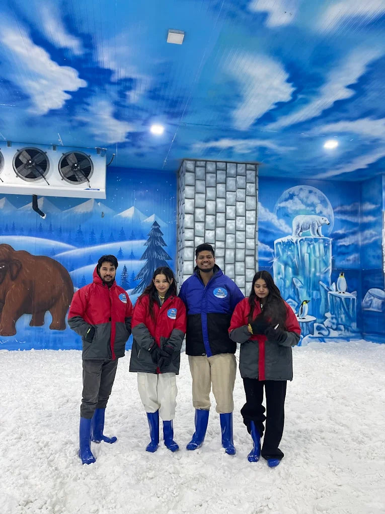 Four young adults in winter gear pose in a snowy indoor park with arctic-themed murals.