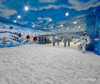People enjoying a snowy indoor ski slope with artificial clouds on the ceiling.