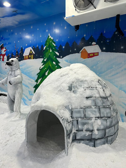 A polar bear stands in front of an igloo in a snowy, winter-themed indoor attraction.