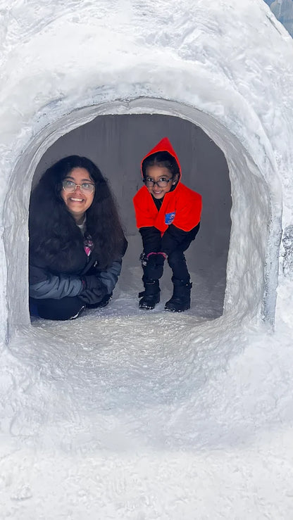 Two young girls smile from inside a snow cave.