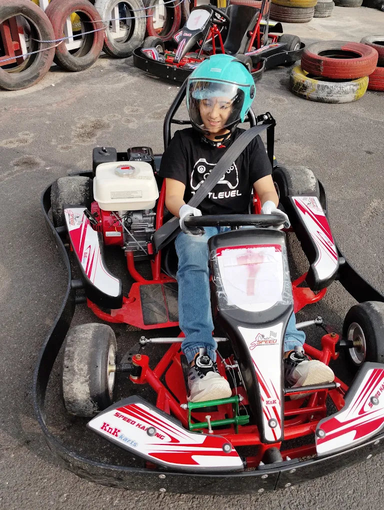 Person sitting in a red and white go-kart on an outdoor track with tires in the background.