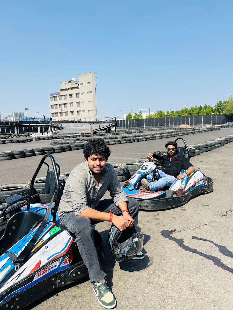 Two young men sit in go-karts on a sunny day at a race track.