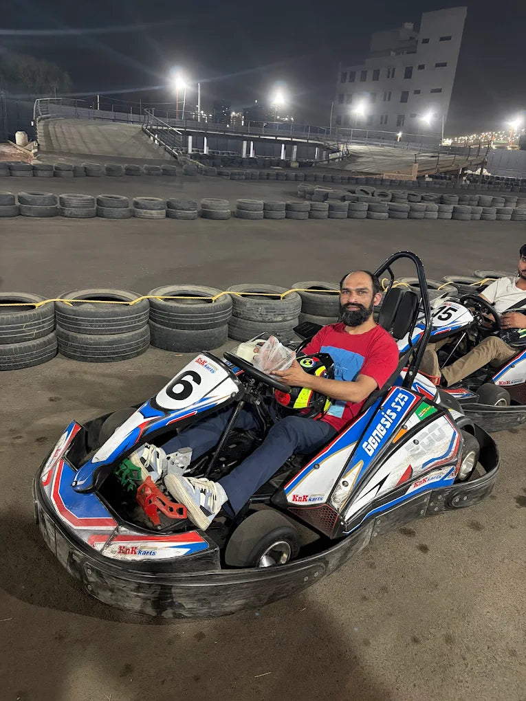 A man in a red shirt sits in a go-kart at a nighttime track, ready to race.
