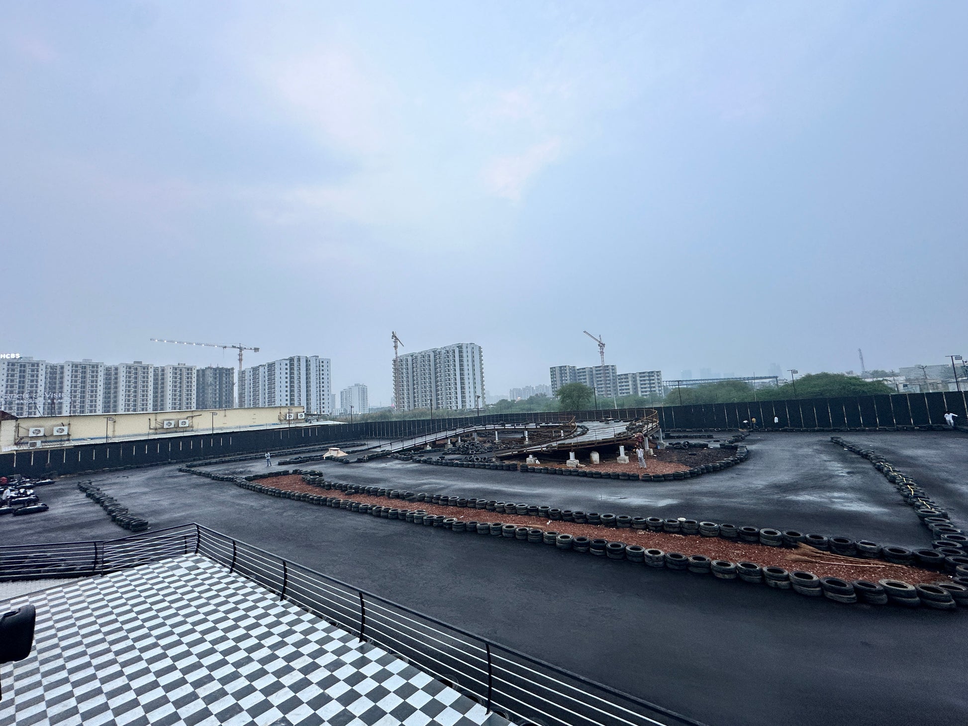 A go-kart track with a checkered floor area and buildings in the background.