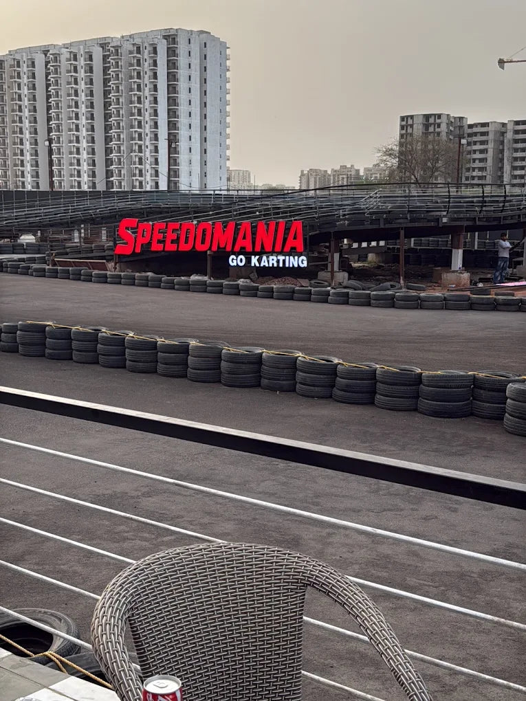A go-karting track with a "SPEEDOMANIA GO KARTING" sign, surrounded by tires and buildings.