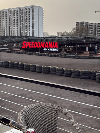 A go-karting track with a "SPEEDOMANIA GO KARTING" sign, surrounded by tires and buildings.
