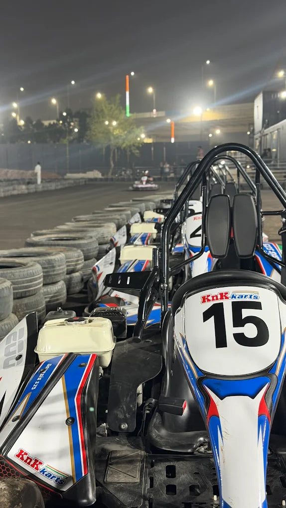 Go-karts lined up at a nighttime track, with a few people visible in the background.