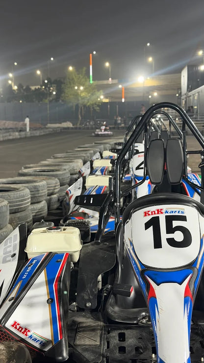 Go-karts lined up at a nighttime track, with a few people visible in the background.