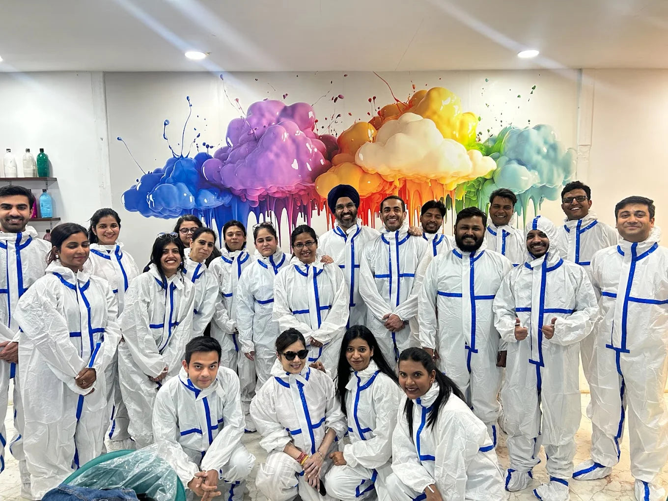 A group of adults in white protective suits pose in front of a colorful, abstract mural.