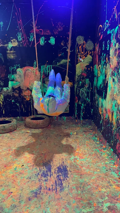 A person swings in a room covered in neon paint splatters under blacklights.