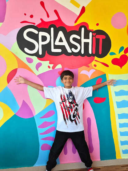 A young boy stands with arms outstretched in front of a colorful mural that says "SPLASH IT".