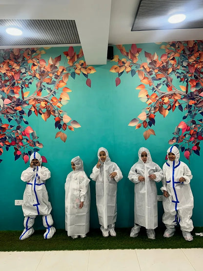 Children in white hazmat suits pose in front of a colorful tree mural.