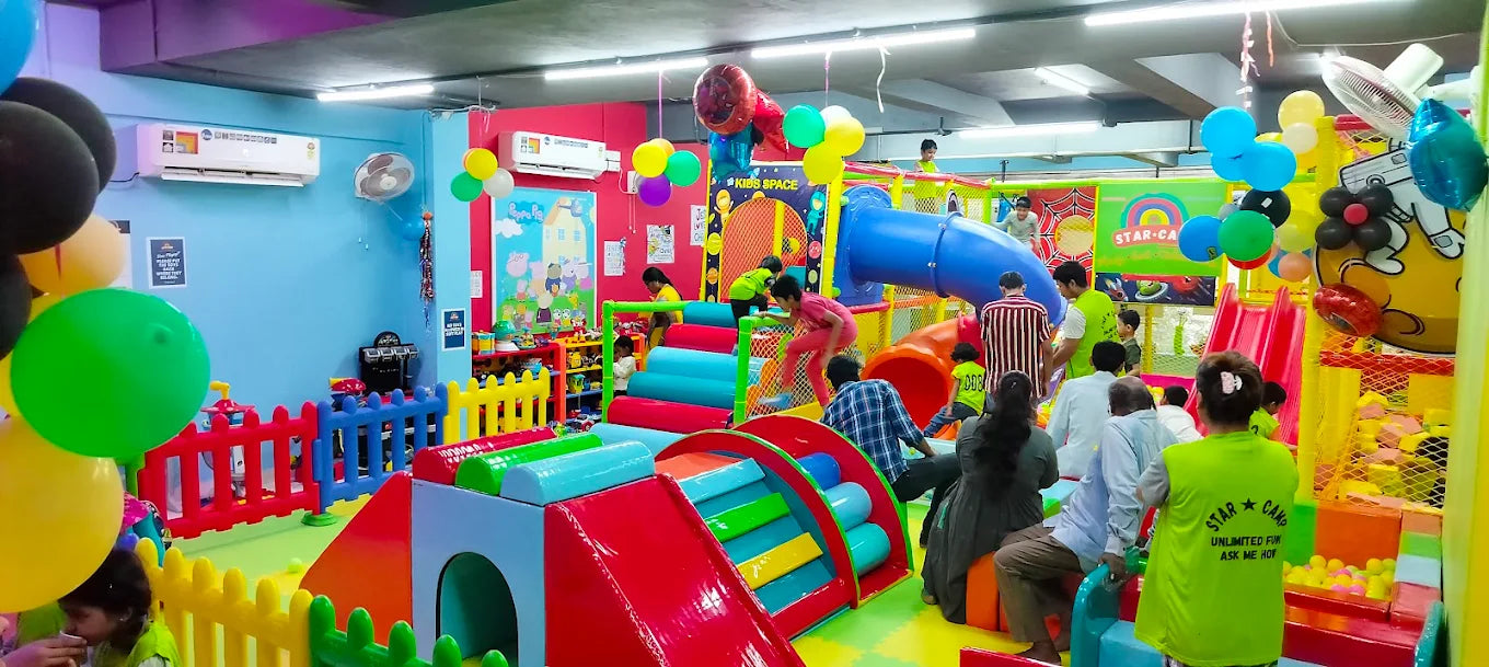 Children play in a colorful indoor playground with slides and ball pits, while adults supervise.