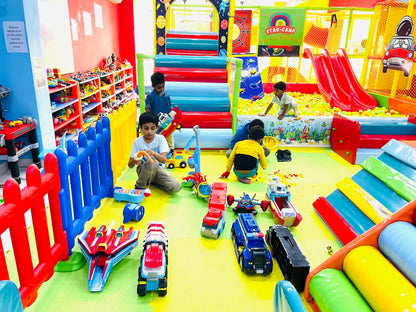 Young children play with toys in a colorful indoor playground with slides and a ball pit.