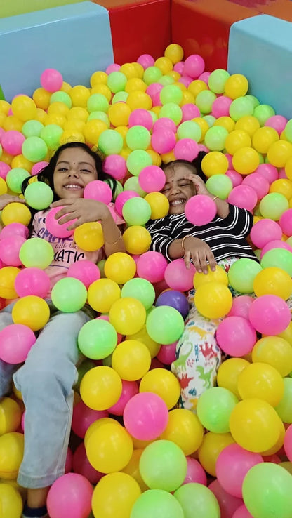 Two young girls smile while playing in a ball pit filled with colorful balls.