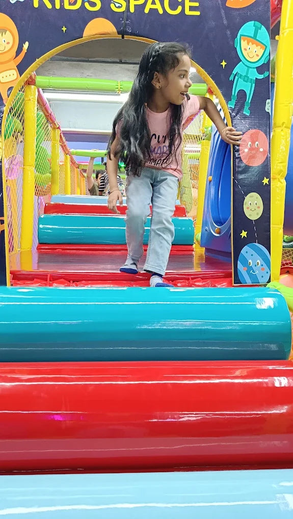 A young girl plays on a colorful indoor playground with space-themed decorations.