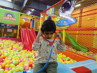 A young child plays doctor with a stethoscope in a colorful ball pit at an indoor playground.