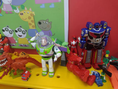 A collection of children's toys, including action figures and stuffed animals, are displayed on a yellow surface.