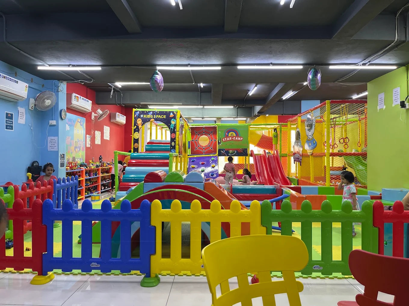 Children play in a colorful indoor playground with slides, ball pits, and climbing structures.