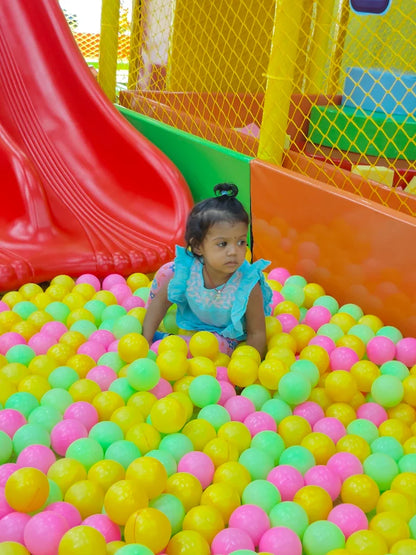 A young child sits in a ball pit with a red slide in the background.
