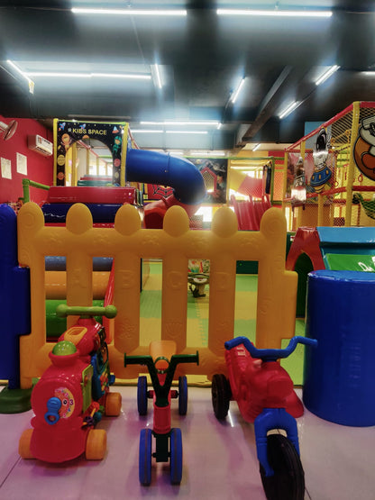A colorful indoor playground with slides and climbing structures, featuring ride-on toys for young children.