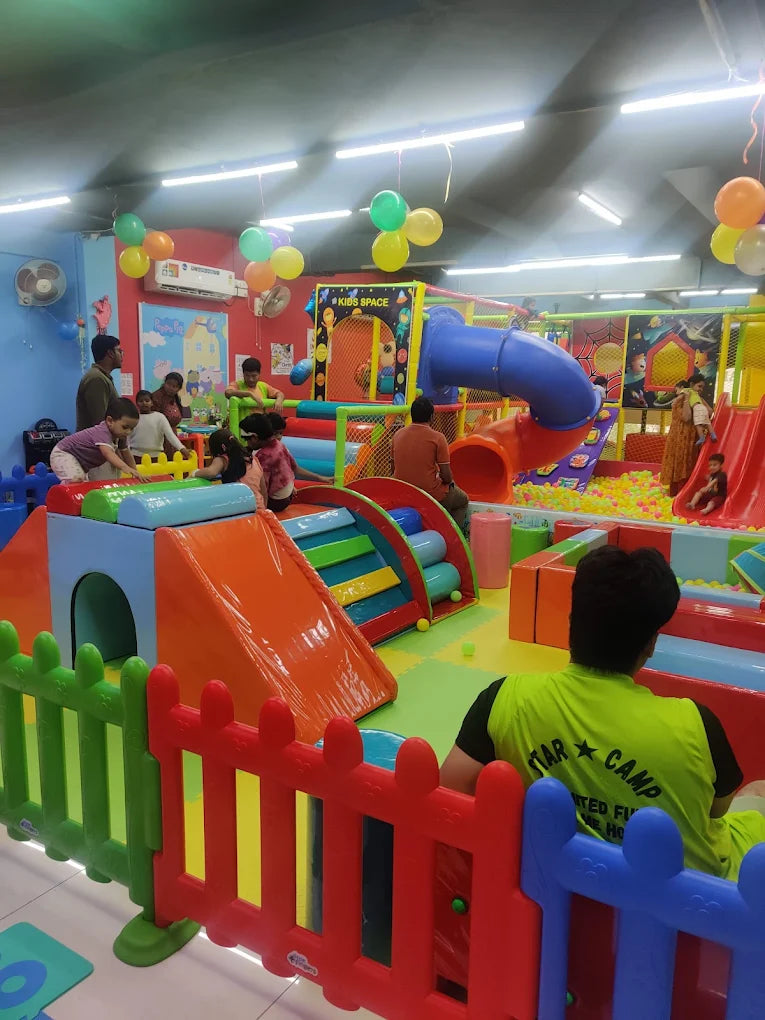 Children play in a colorful indoor playground with slides and ball pits. Adults supervise the kids in the fun-filled space.
