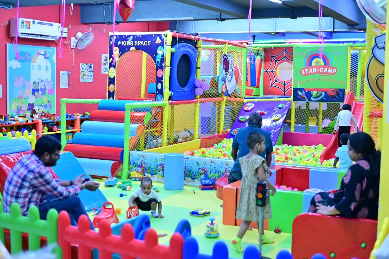 A colorful indoor playground with children and adults enjoying the ball pit and climbing structures.