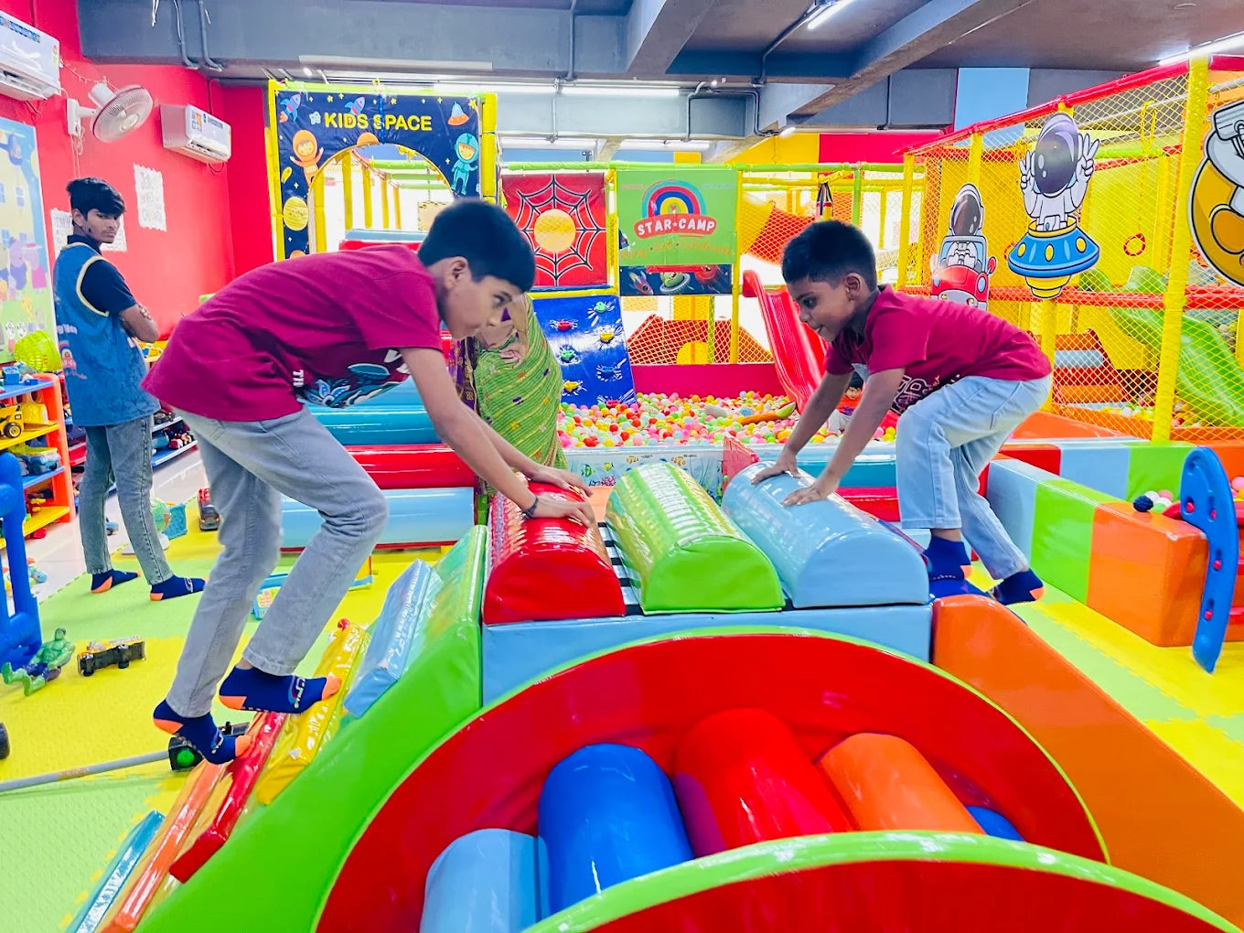 Children play in a colorful indoor playground with ball pits and soft climbing structures.
