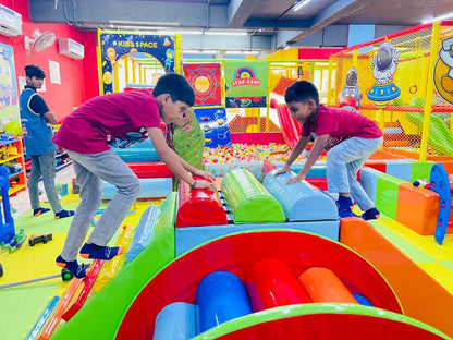 Children play in a colorful indoor playground with ball pits and soft climbing structures.