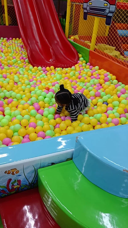 A toddler plays in a ball pit with a red slide.
