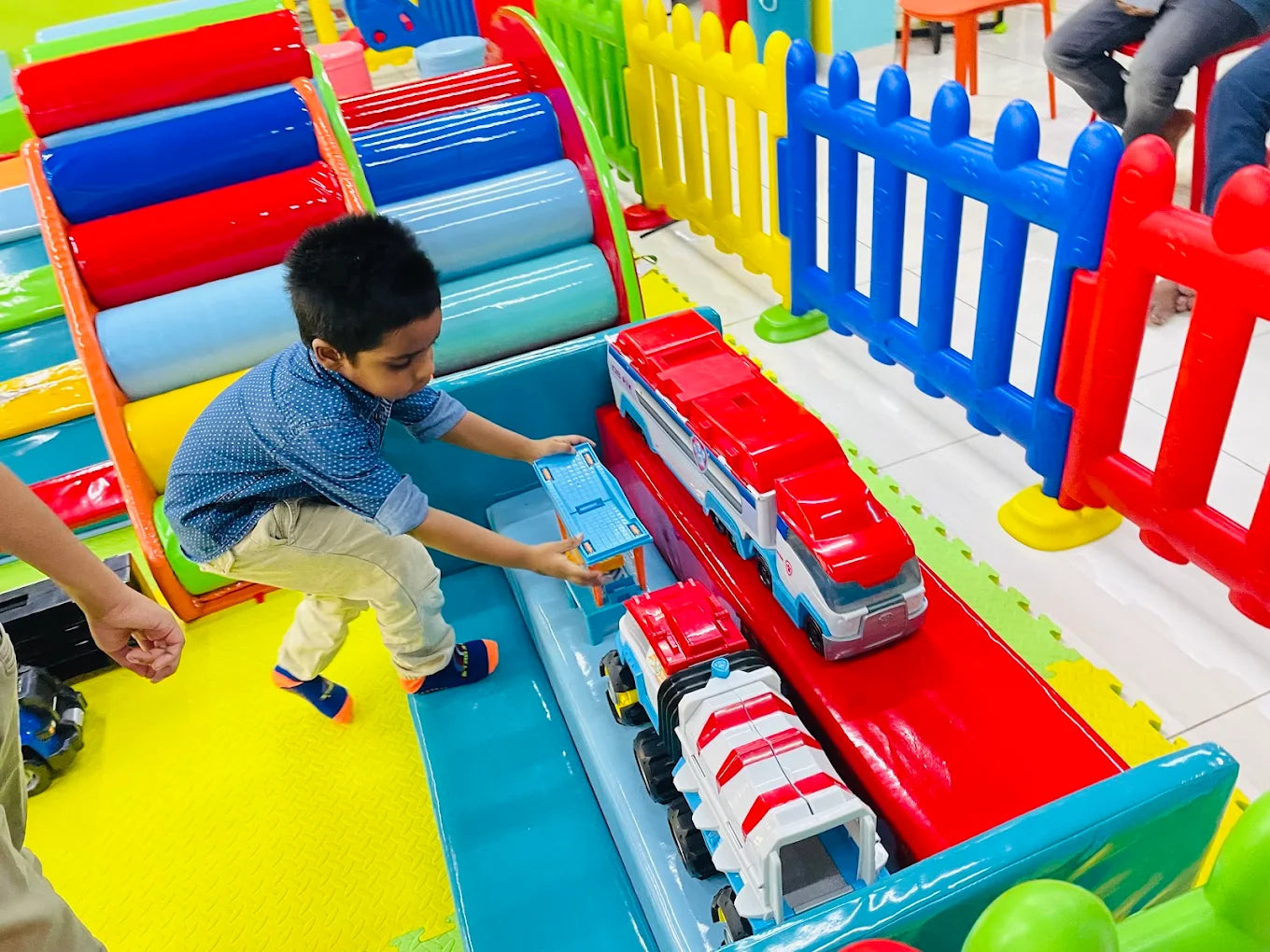 A young boy plays with toy trucks on a colorful indoor playground.