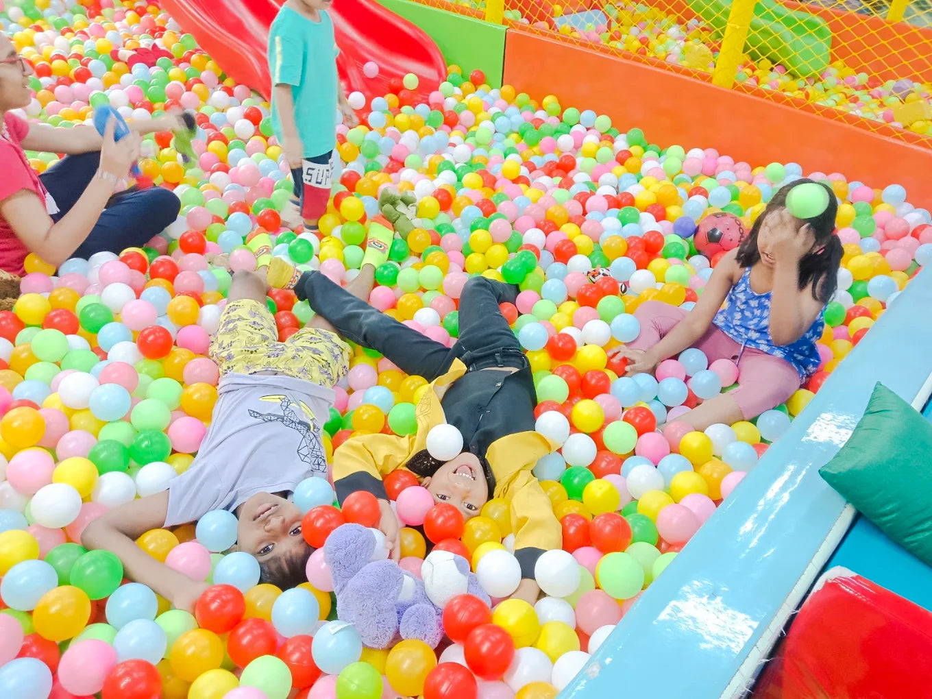 Children play in a colorful ball pit, with some lying down and others sitting.