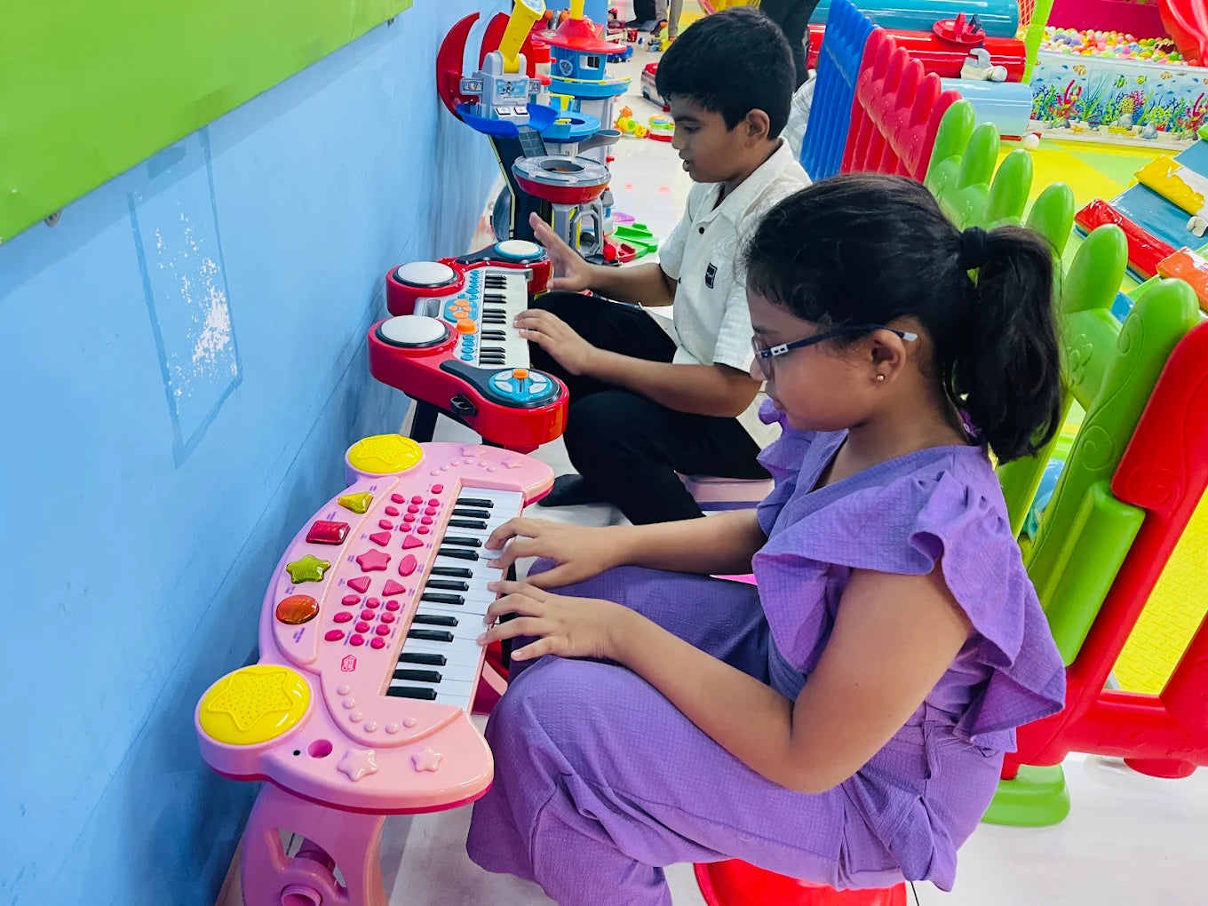 Two children play toy keyboards in a colorful playroom.