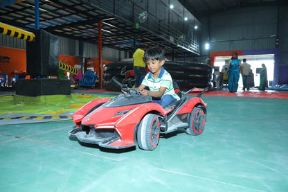 A young boy drives a red toy car in an indoor amusement park.