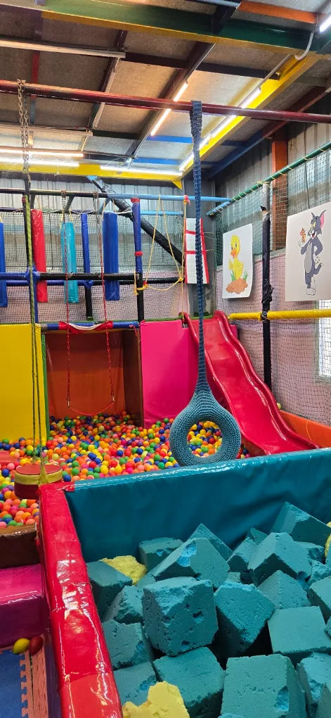 A colorful indoor playground with a ball pit, slide, and foam blocks, designed for children.