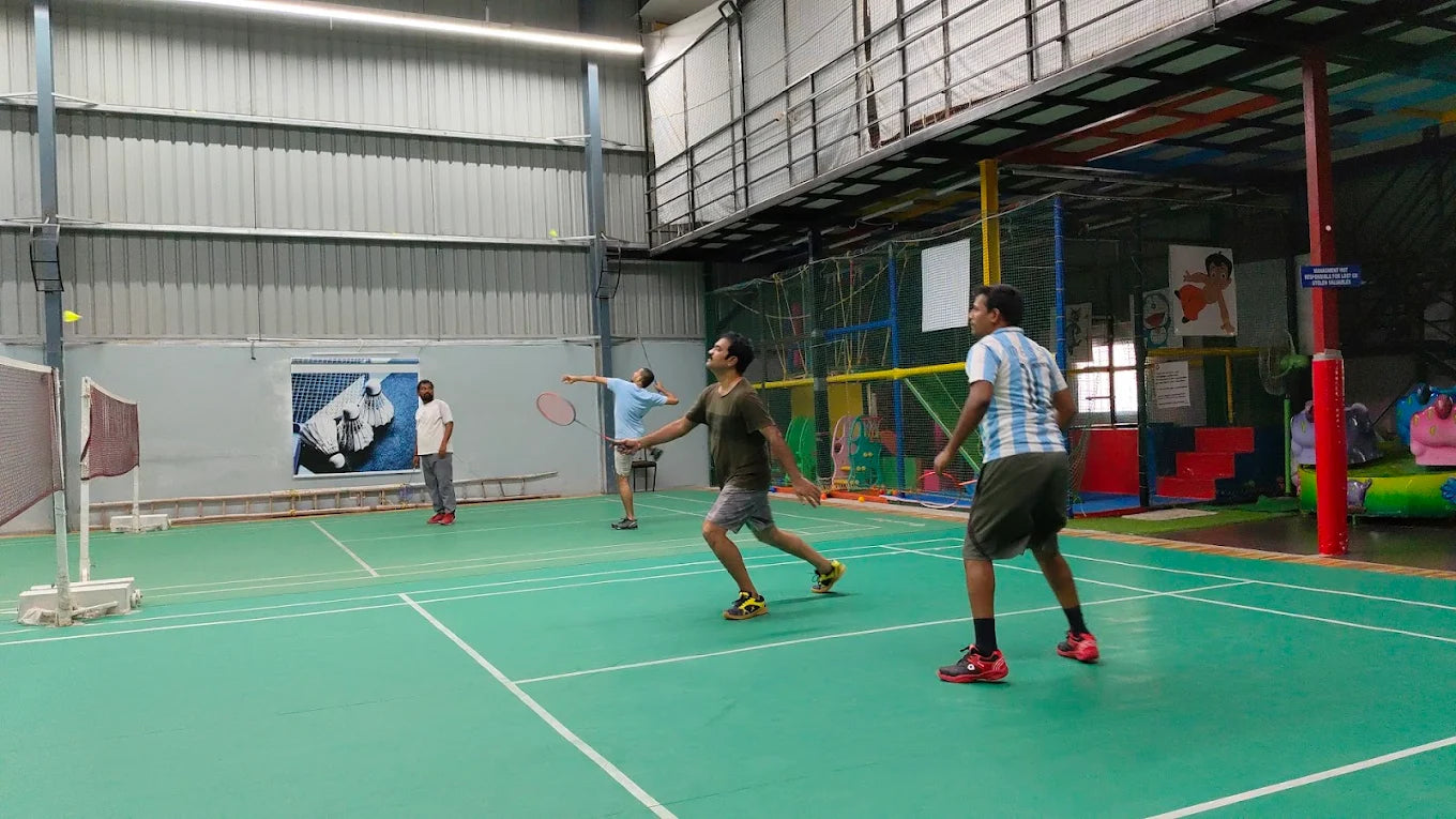 Adults playing badminton indoors on a green court.
