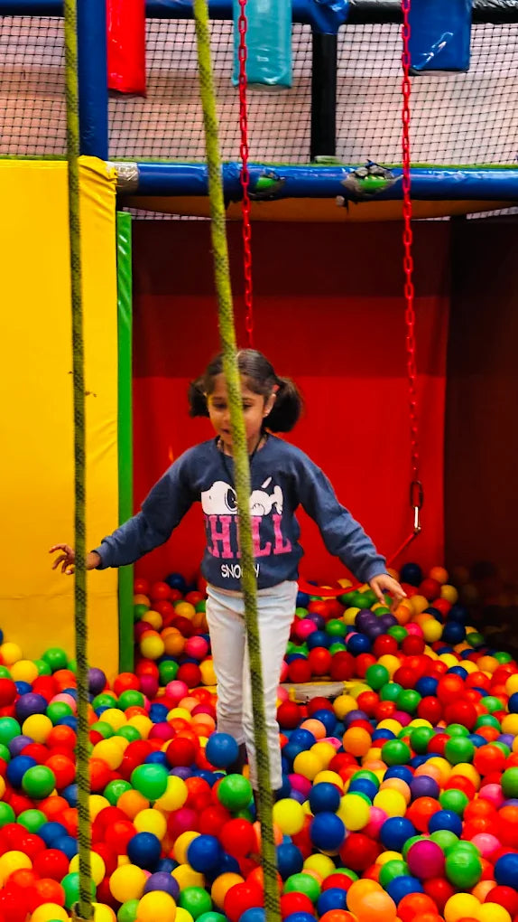 A young girl stands in a ball pit, surrounded by colorful balls.