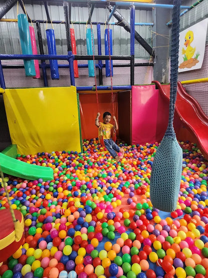 A young boy swings on a swing over a ball pit in an indoor playground.