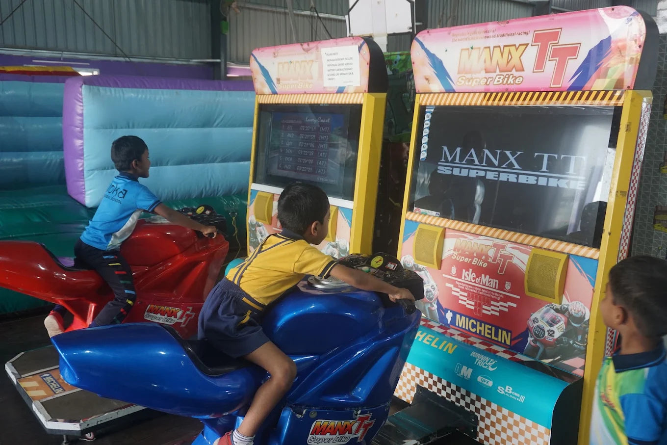 Two young boys play a motorcycle racing arcade game in an indoor play area.