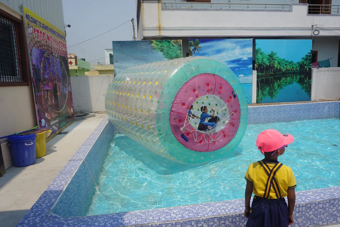 Children play inside a giant inflatable ball in a pool, with another child watching.