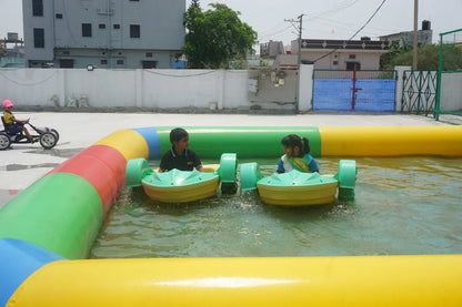 Children enjoy riding bumper boats in a colorful inflatable pool. Another child rides a pedal car nearby.